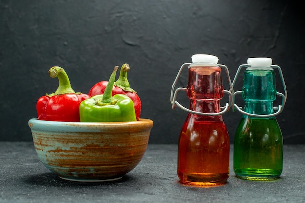 Gratis foto zijaanzicht van kom paprika's aan de linkerkant met flessen olie en azijn aan de zijkant op donkergrijze tafel