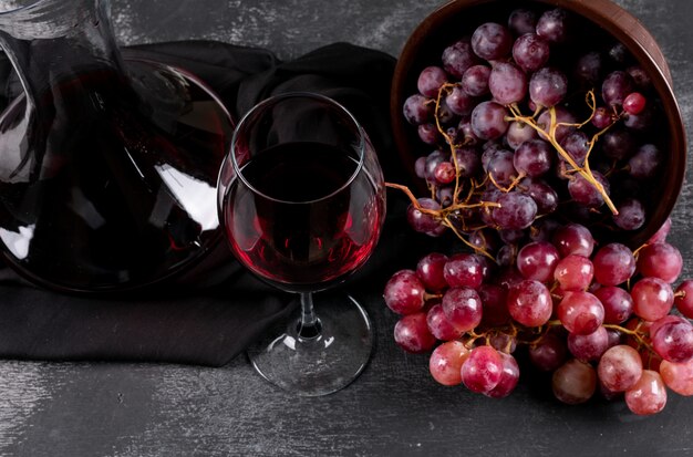 Zijaanzicht van kruik met rode wijn en druif op donkere horizontaal