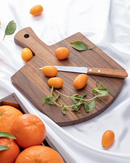Zijaanzicht van kumquats met bladeren en mes op snijplank en sinaasappels met grapefruits op witte achtergrond