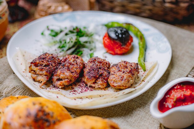 Zijaanzicht van lula kebab met sumak uikruiden en geroosterde groenten op lavash in een witte plaat