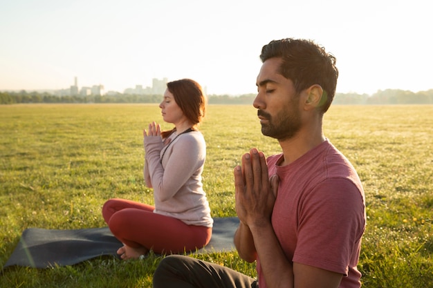 Zijaanzicht van man en vrouw die buiten mediteren op yogamatten