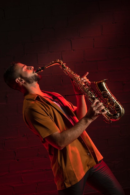Gratis foto zijaanzicht van mannelijke artiest die de saxofoon speelt
