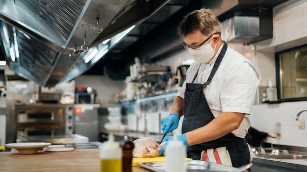 Gratis foto zijaanzicht van mannelijke chef-kok met masker scherpe kip