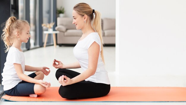 Zijaanzicht van moeder en dochter die yoga thuis met exemplaarruimte doen
