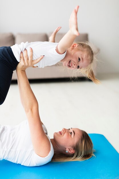 Zijaanzicht van moeder op yogamat die gelukkige dochter opheft