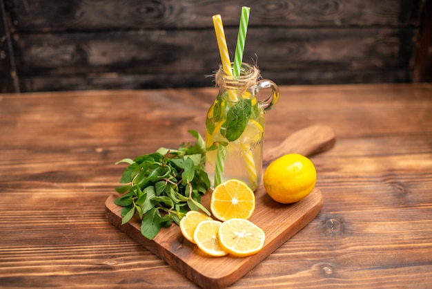 Zijaanzicht van natuurlijk vers detoxwater geserveerd met buisjes munt en sinaasappel op een houten tafel