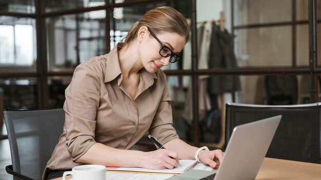 Zijaanzicht van onderneemster die met laptop bij bureau werkt