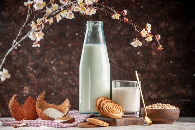 Zijaanzicht van open glazen fles en beker gevuld met melklepel koekjes haver in bruine pot op paarse gestripte handdoek op houten snijplank