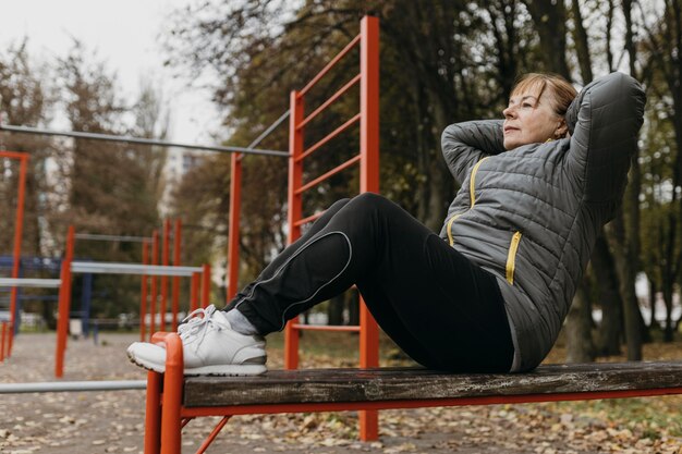 Zijaanzicht van oudere vrouw die crunches buitenshuis doet