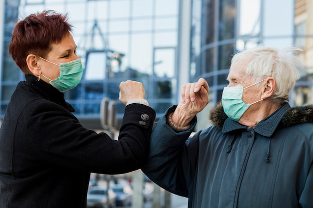 Gratis foto zijaanzicht van oudere vrouwen die ellebogen gebruiken om elkaar te groeten terwijl ze medische maskers dragen