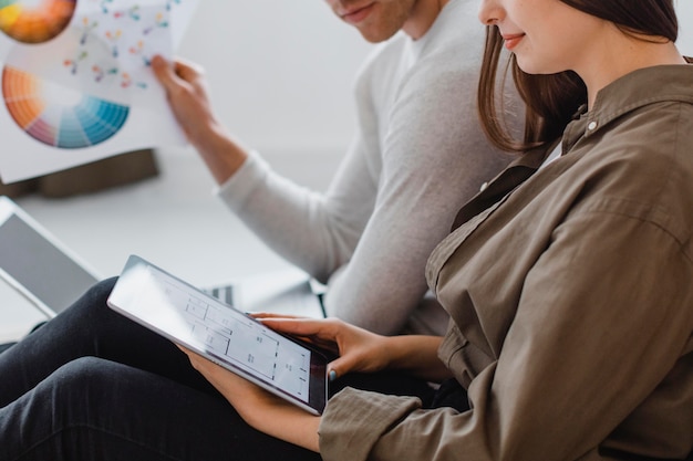 Zijaanzicht van paar dat van plan is het huis opnieuw in te richten met behulp van tablet en verfpalet