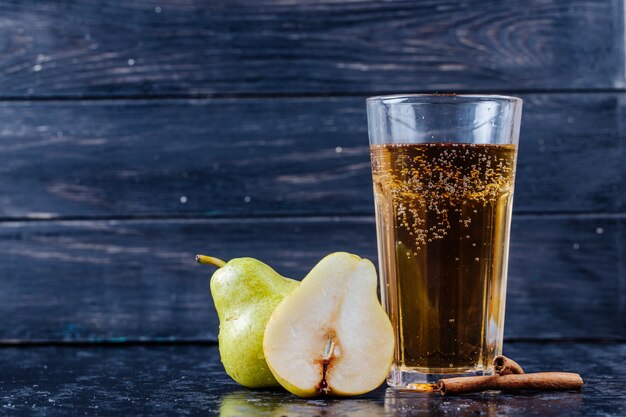 Zijaanzicht van perenlimonade in een glas met de verse perenhelften bij zwarte houten achtergrond