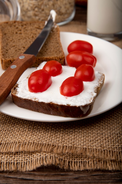 Zijaanzicht van plaat met de plakkwark van het roggebrood en tomaten met mes op juteoppervlakte