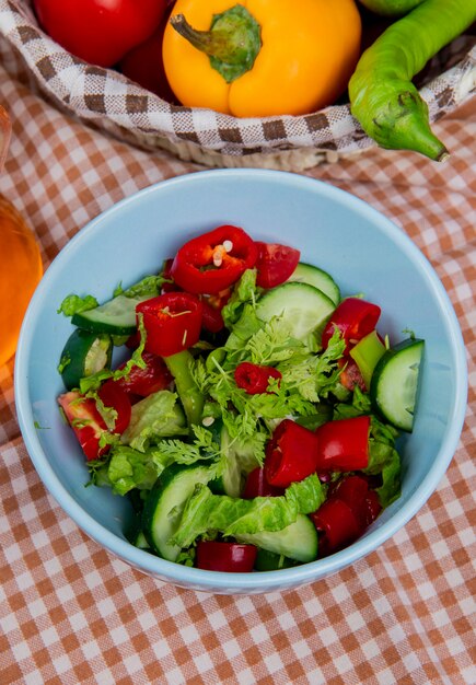 Zijaanzicht van plantaardige salade in kom met groenten in mand op geruite doek