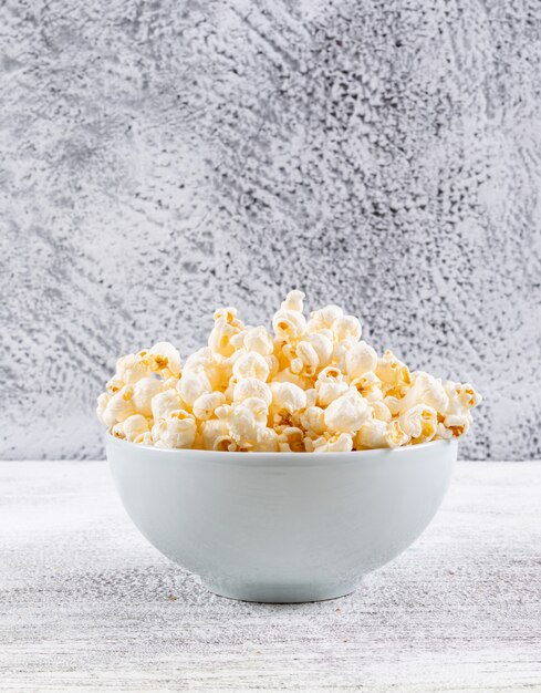 Zijaanzicht van popcorn in kom op witte houten lijstverticaal