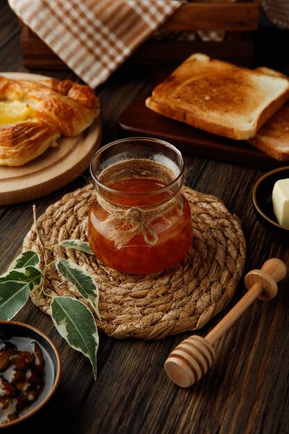 Zijaanzicht van pot kweepeerjam op onderzetter met gedroogd brood, sneetjes croissant op houten achtergrond