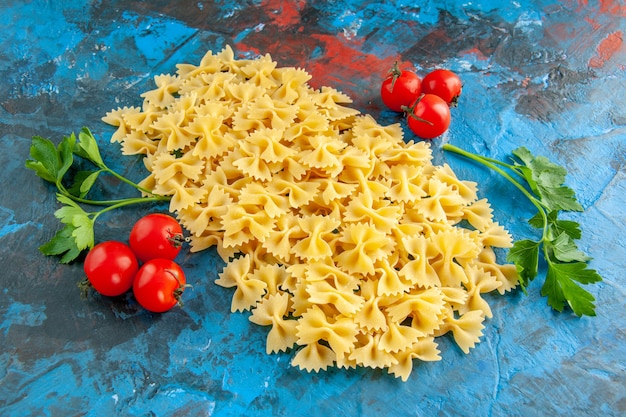 Zijaanzicht van rauwe farfalle pasta's en tomaten met stengel groen op blauwe achtergrond