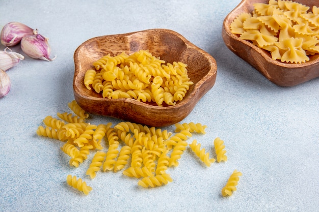 Zijaanzicht van rauwe pasta in een kom met knoflook op een wit oppervlak