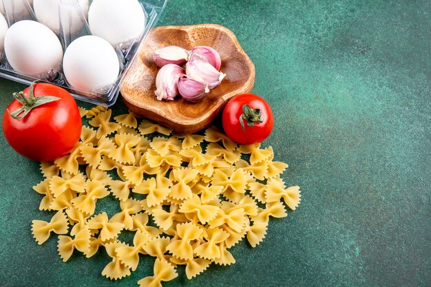 Zijaanzicht van rauwe pasta met knoflooktomaatjes en eieren op een groene ondergrond