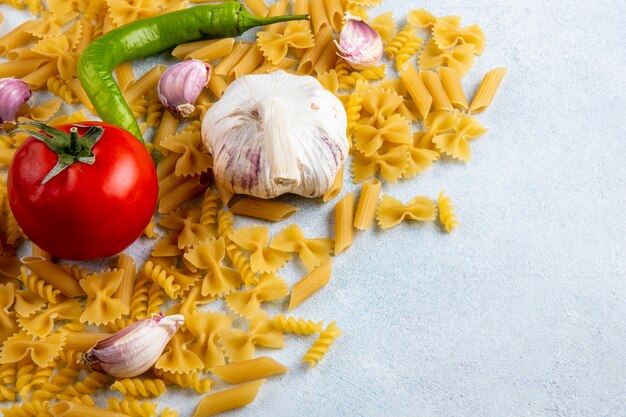 Zijaanzicht van rauwe pasta met tomaten, knoflook en chilipepers op een grijze ondergrond