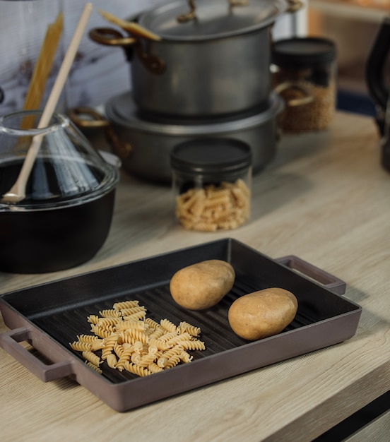 Zijaanzicht van rauwe spiraal pasta en twee aardappelen in een pan op een keukentafel