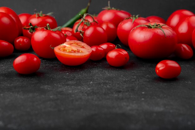 Zijaanzicht van rijpe verse tomaten die op zwarte achtergrond met exemplaarruimte worden verspreid