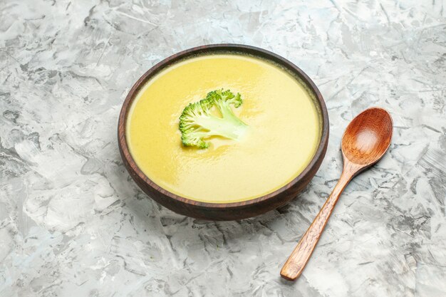 Zijaanzicht van romige broccolisoep in een bruine kom en lepel op grijze lijst