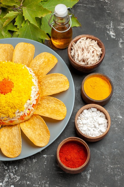 Zijaanzicht van salade met kruidenoliefles en bladeren aan de zijkant op donkergrijze tafel