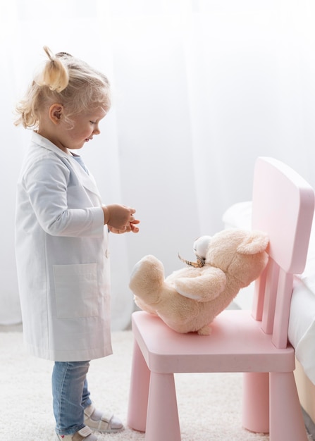 Gratis foto zijaanzicht van schattige peuter met laboratoriumjas en teddybeer