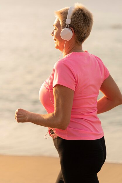 Zijaanzicht van senior vrouw met koptelefoon joggen op het strand