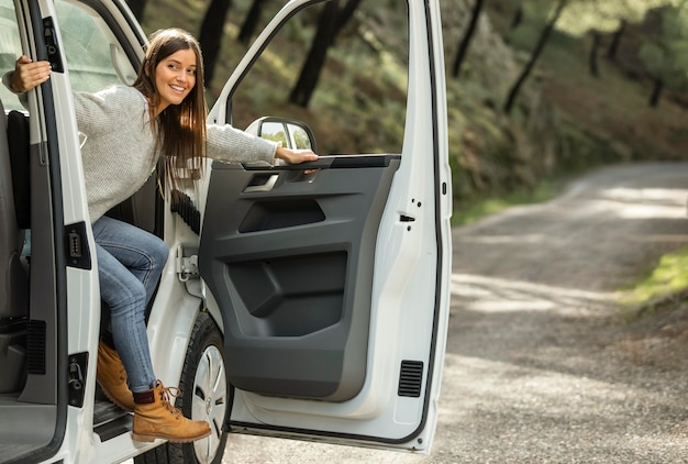 Zijaanzicht van smileyvrouw die tijdens een roadtrip uit de auto stappen