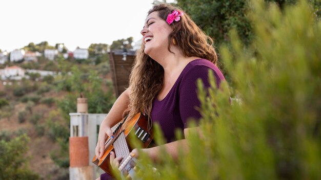 Zijaanzicht van smileyvrouw in openlucht met gitaar