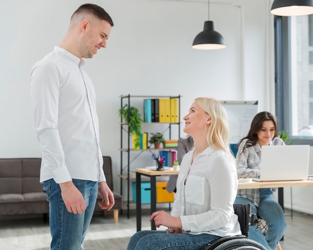 Zijaanzicht van smileyvrouw in rolstoel die met medewerker converseren