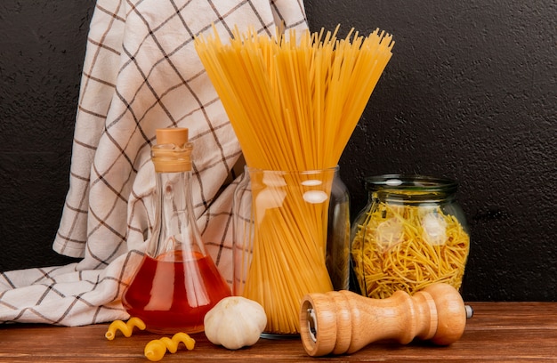 Zijaanzicht van spaghettideegwaren in kruiken met gesmolten boterzout van het knoflook en geruite doek op houten oppervlakte