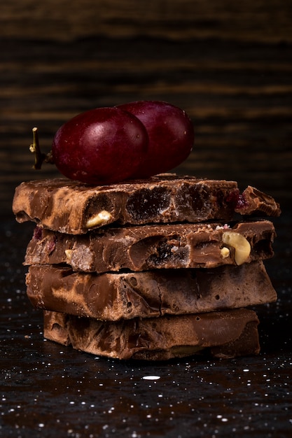 Zijaanzicht van stapel melk en donkere chocolade met notenvruchten en bessen en pijpjes kaneel op donkere achtergrond