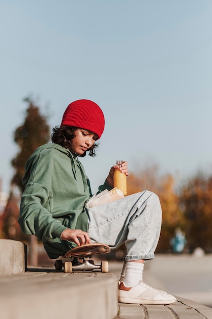 Gratis foto zijaanzicht van tiener die lunch in het park op skateboard heeft