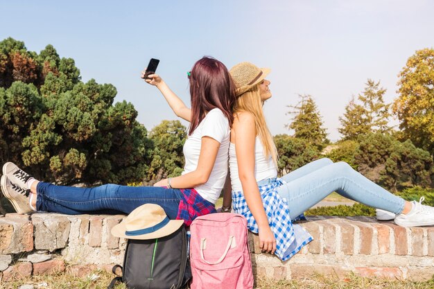 Gratis foto zijaanzicht van twee vrouwelijke vrienden die het rijtjes nemen zitten selfie op cellphone