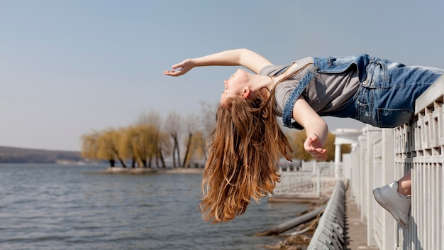 Gratis foto zijaanzicht van van zorgeloze vrouw die achteruit op traliewerk leunt