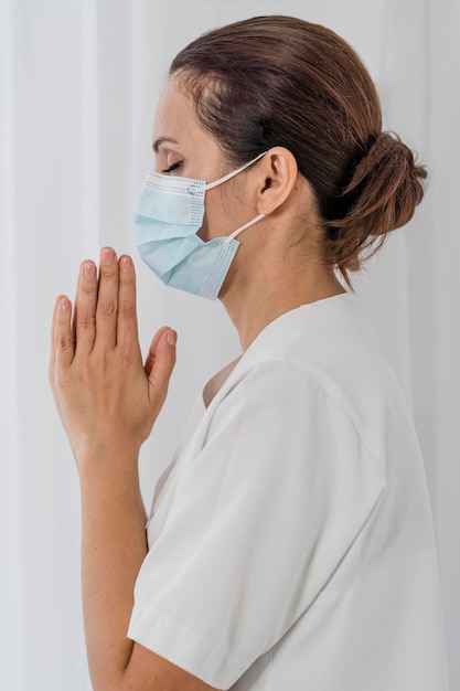 Zijaanzicht van verpleegster met medisch masker bidden