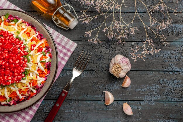 Zijaanzicht van verre plaat en vork boomtakken knoflook fles olie en schotel op het geruite tafelkleed naast de vork op tafel