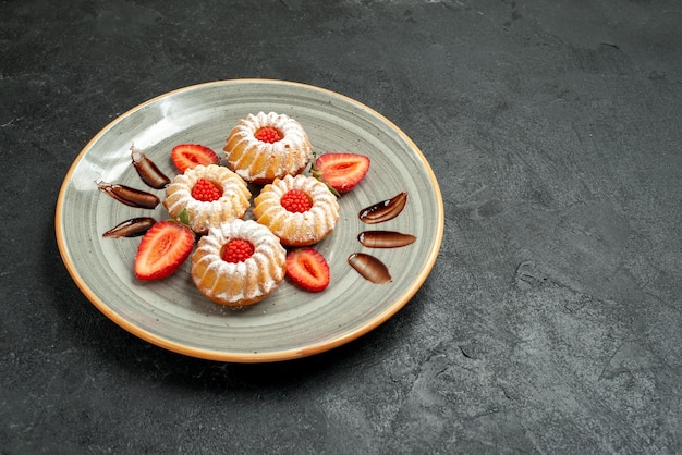 Zijaanzicht van verre smakelijke koekjeskoekjes met chocolade en aardbei in bord aan de linkerkant van tafel