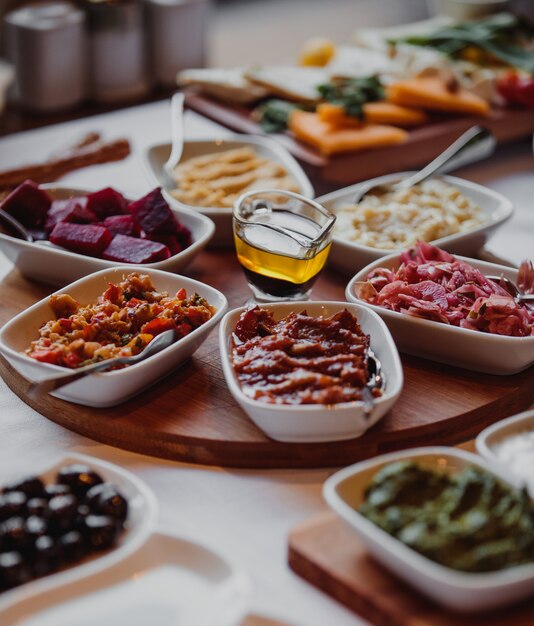 Zijaanzicht van verschillende sauzen en salades met groenten op een houten plank en olijfolie in het midden