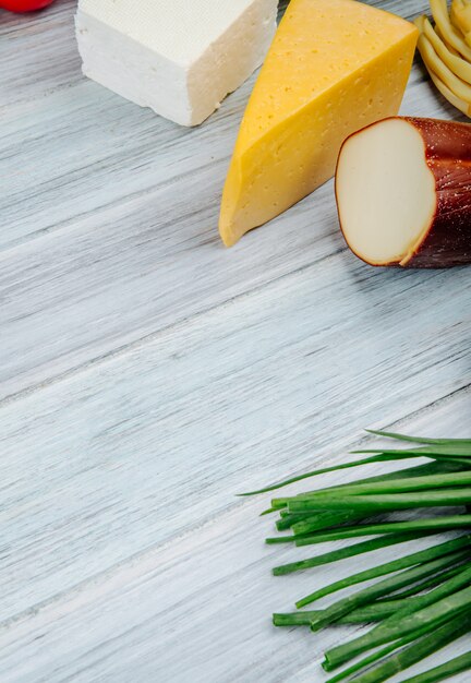 Zijaanzicht van verschillende soorten kaas met groene ui op grijze houten tafel met kopie ruimte