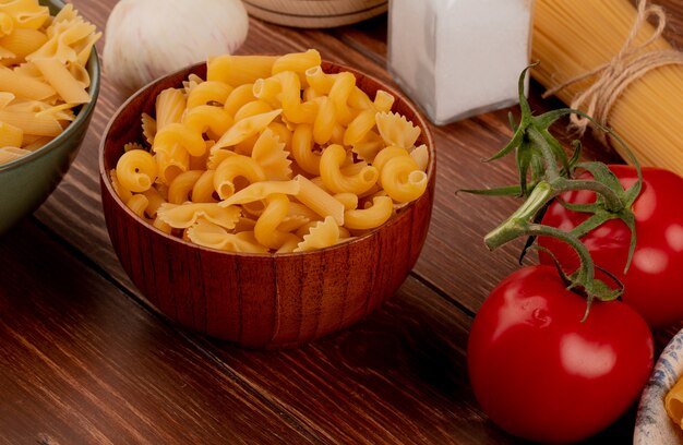 Zijaanzicht van verschillende soorten macaroni in kommen en zout tomaten knoflook op houten tafel
