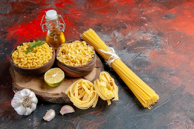 Zijaanzicht van verschillende soorten ongekookte pasta's en knoflookcitroenoliefles op gemengde kleurenachtergrond