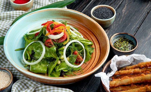 zijaanzicht van verse groentesalade in een plaat geserveerd met sojasaus en zwarte zaden op houten tafel