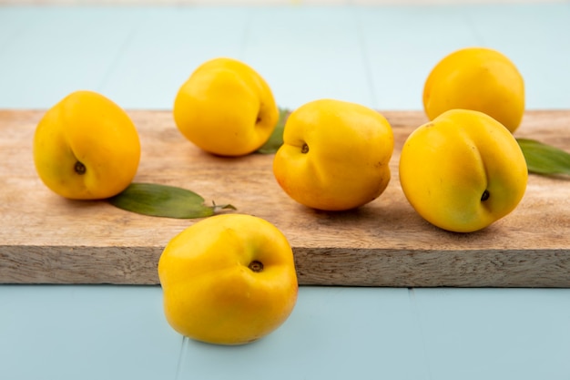 Zijaanzicht van verse heerlijke gele perziken op een houten keukenbord op een blauwe achtergrond