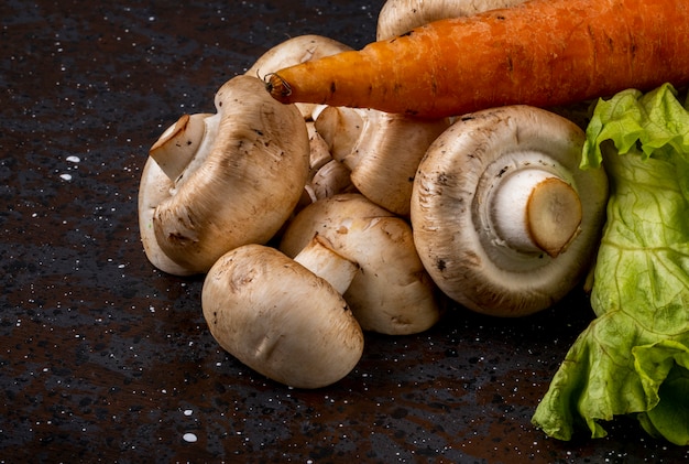 Zijaanzicht van verse paddestoelenchampignon en wortel op donkere achtergrond