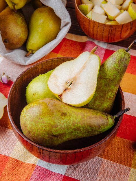 Zijaanzicht van verse rijpe peren en de helft in een houten kom op plaidachtergrond