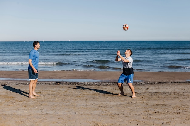 Gratis foto zijaanzicht van vrienden die voetbal spelen bij het strand
